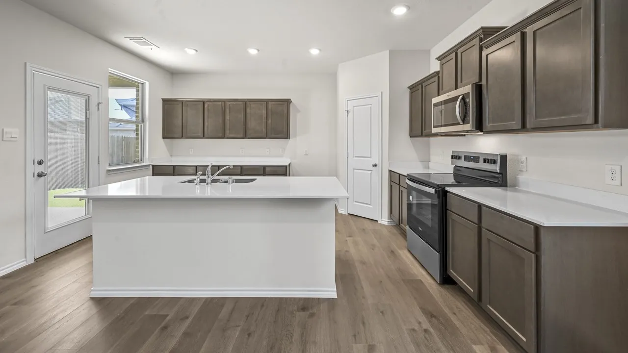 Kitchen featuring a central island with an integrated sink, wood-finish flooring, stainless steel appliances, white countertops, and recessed lighting