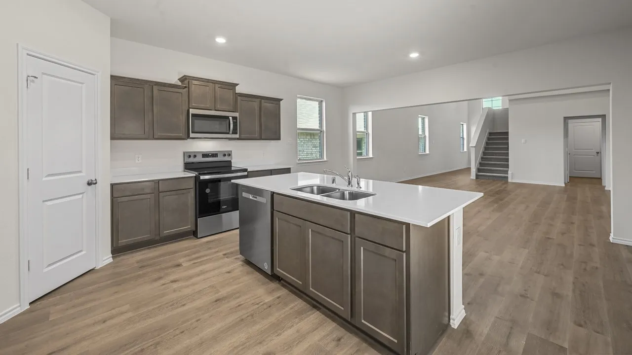 Spacious kitchen featuring an island with a double basin sink, stainless steel appliances, dark wood-finish cabinetry, and light-tone wood-finish flooring