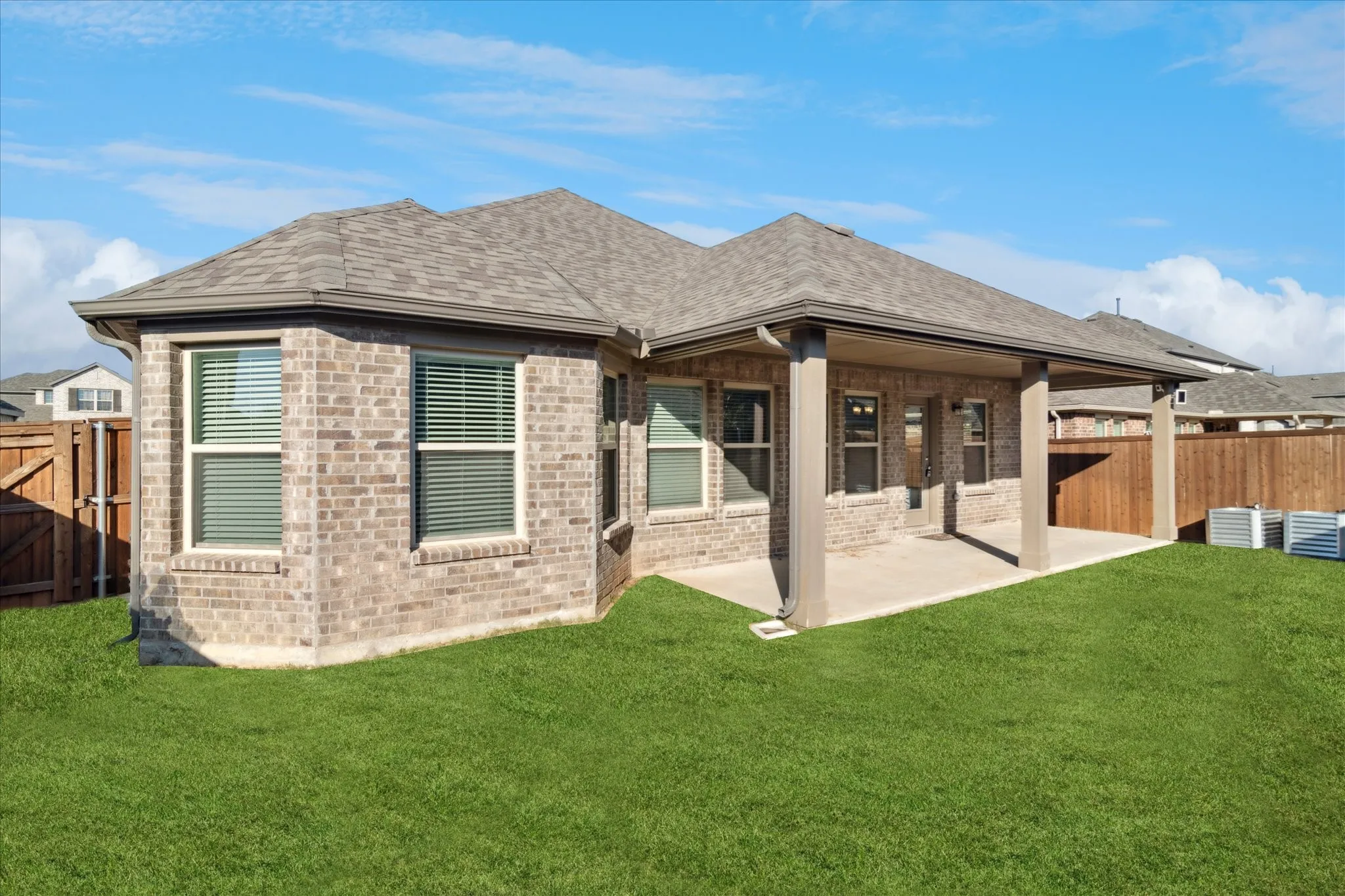 Expansive green lawn with a covered patio featuring substantial support columns, a brick exterior, and a shingled roof