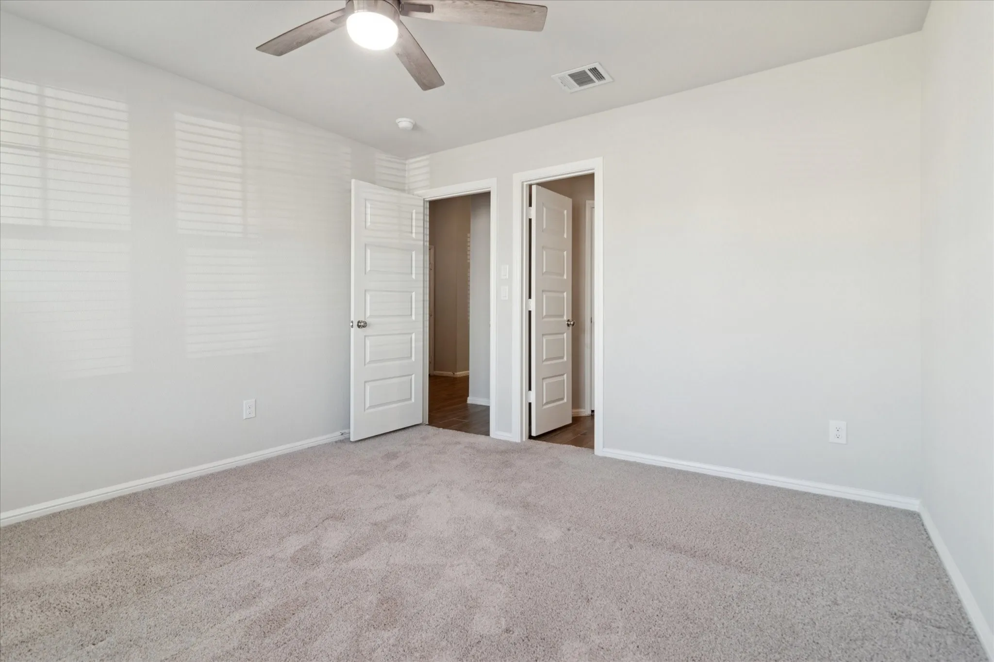 Neutral wall color, ceiling fan, window with blinds, and light-toned carpeting