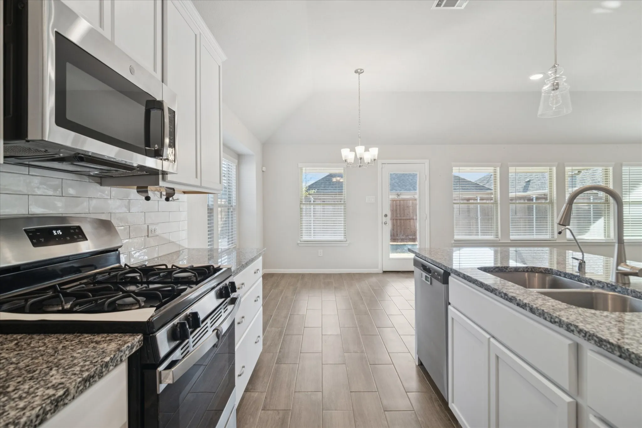 Kitchen featuring stainless steel appliances, granite countertops, white cabinetry, a subway tile backsplash, and wood-finish flooring