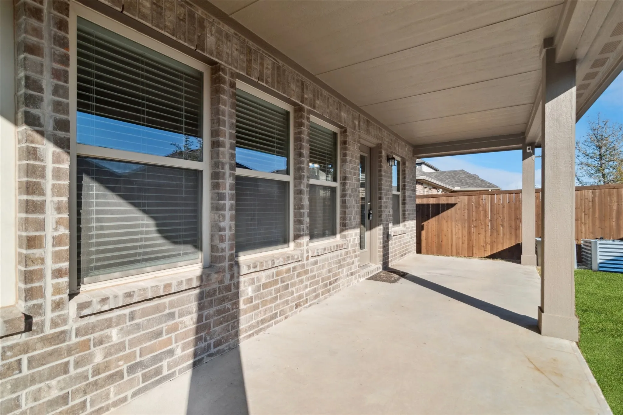 Covered patio featuring a concrete surface, exposed brick exterior, and multiple windows