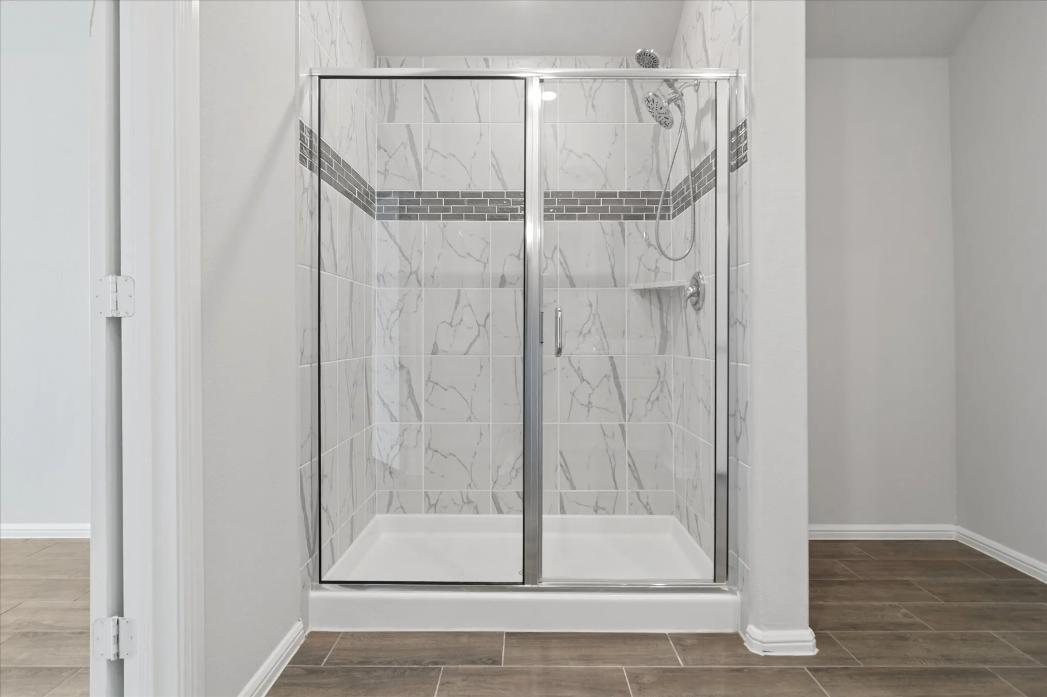 Shower enclosure with glass paneling, white marble-look tile, mosaic accent band, built-in shelving, and a dual-head shower system