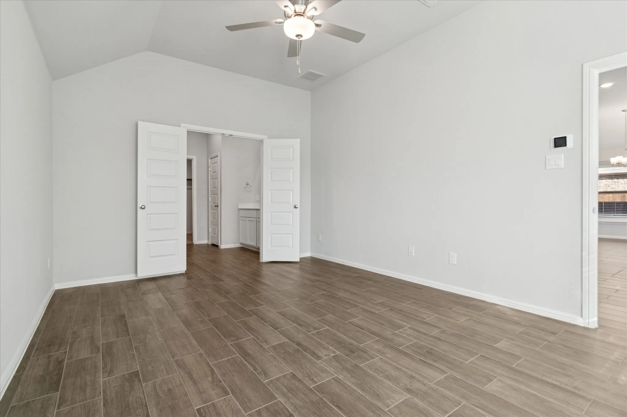 Vaulted ceiling with a ceiling fan, wood-finish flooring, white paneled doors, and light-toned walls