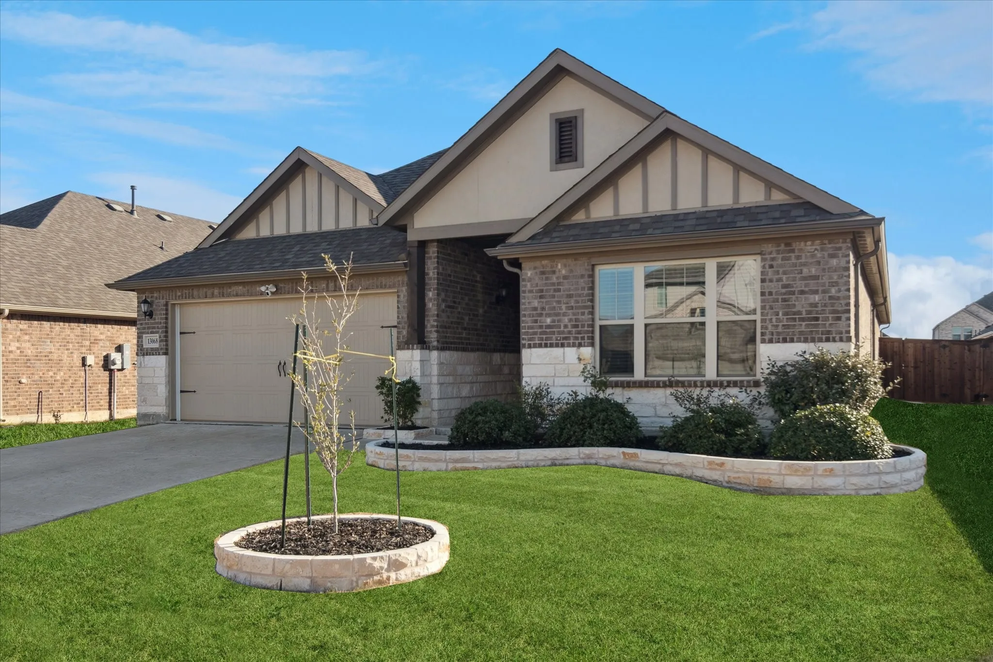 Brick and stone facade with a gable roof, concrete driveway, and landscaped front yard with a curved stone planter