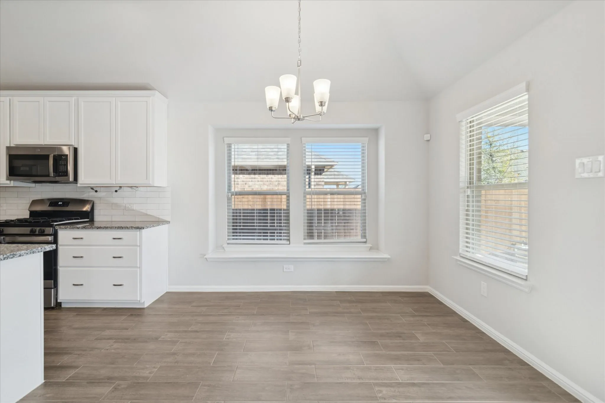 Kitchen and dining area featuring white cabinetry, stainless steel appliances, granite countertops, tile backsplash, and wood-finish flooring