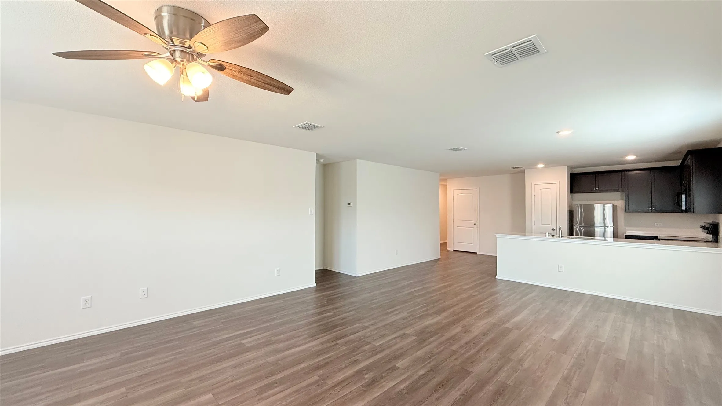 Wood-finish flooring, ceiling fan with integrated lighting, recessed lighting, white walls, and dark wood-finish cabinetry