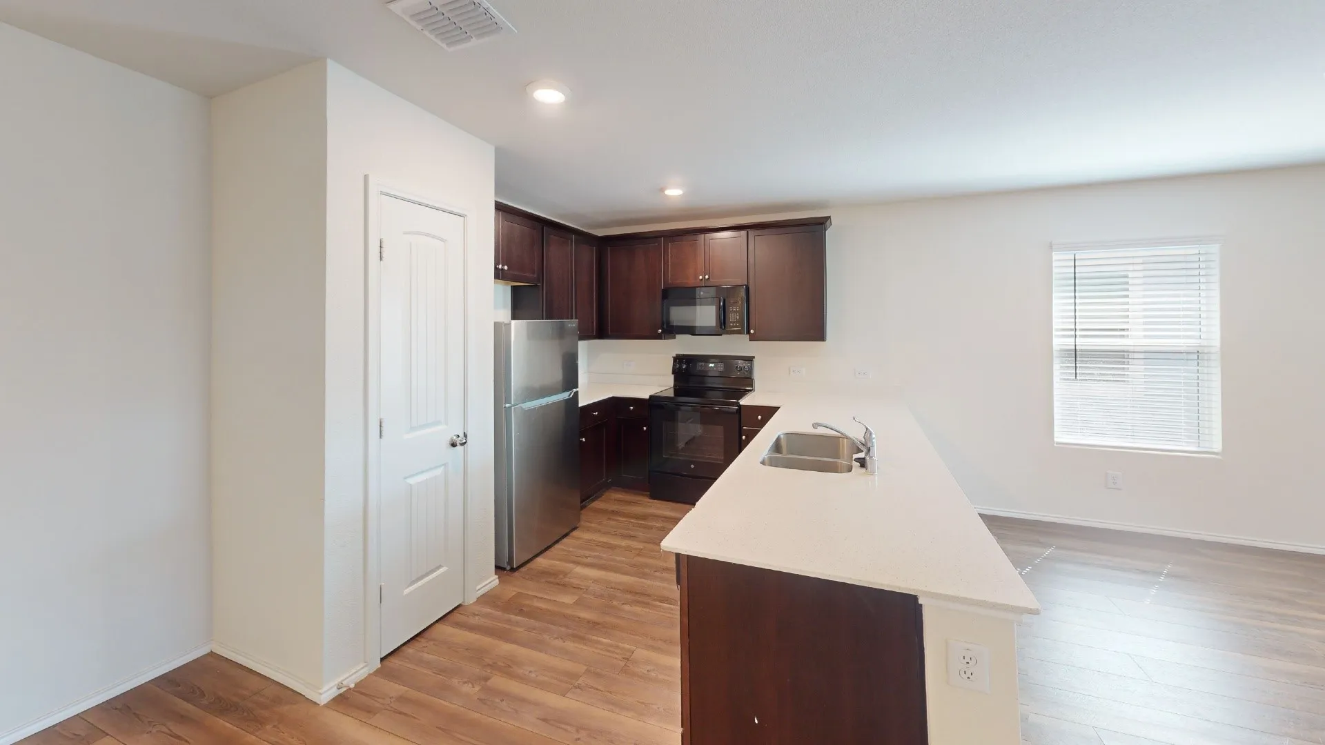 Kitchen featuring dark wood-finish cabinetry, stainless steel refrigerator, black range, and an expansive island with a stainless steel sink