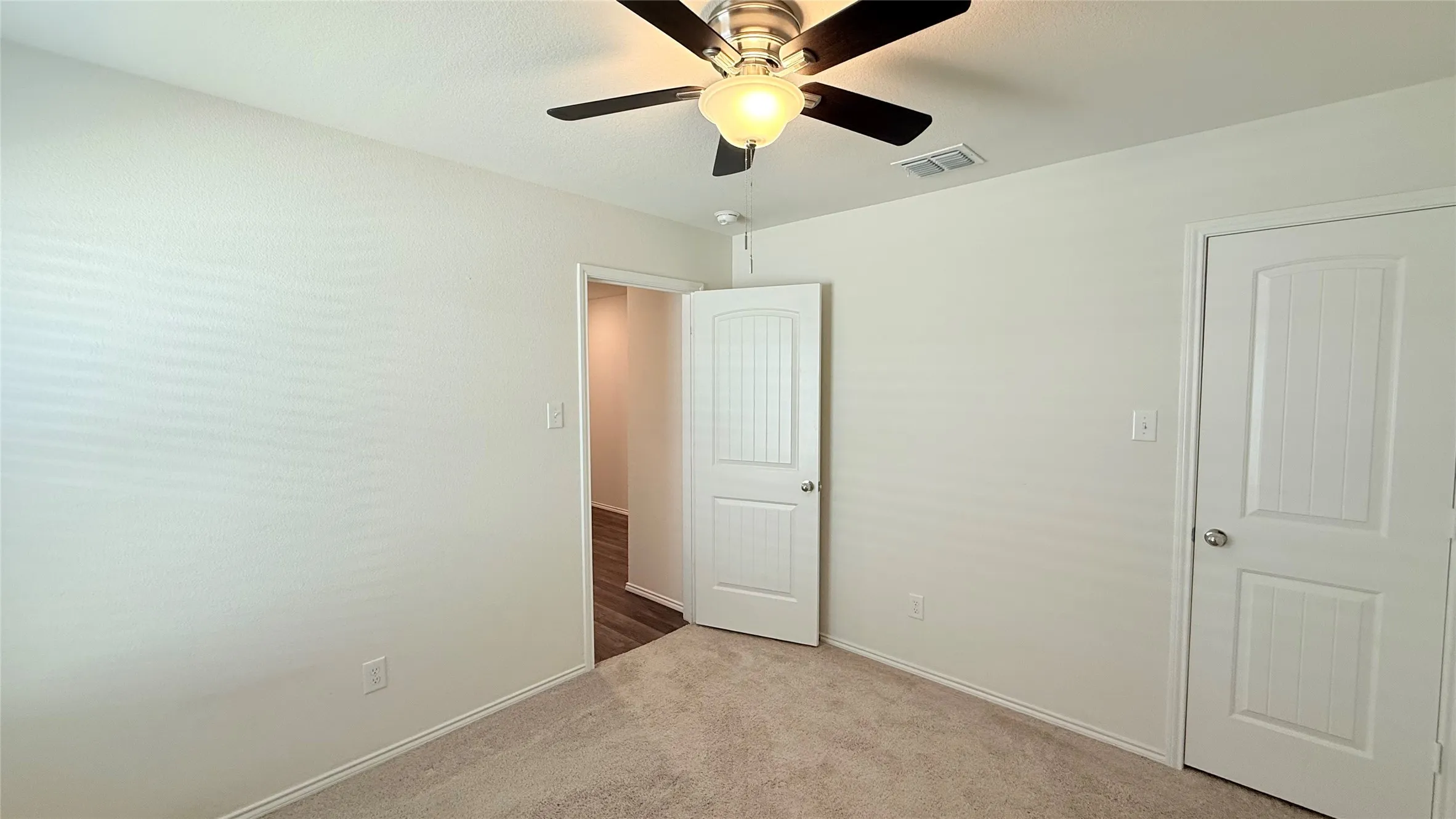 Neutral wall paint, carpet flooring, a ceiling fan with integrated lighting, and two paneled doors with hardware