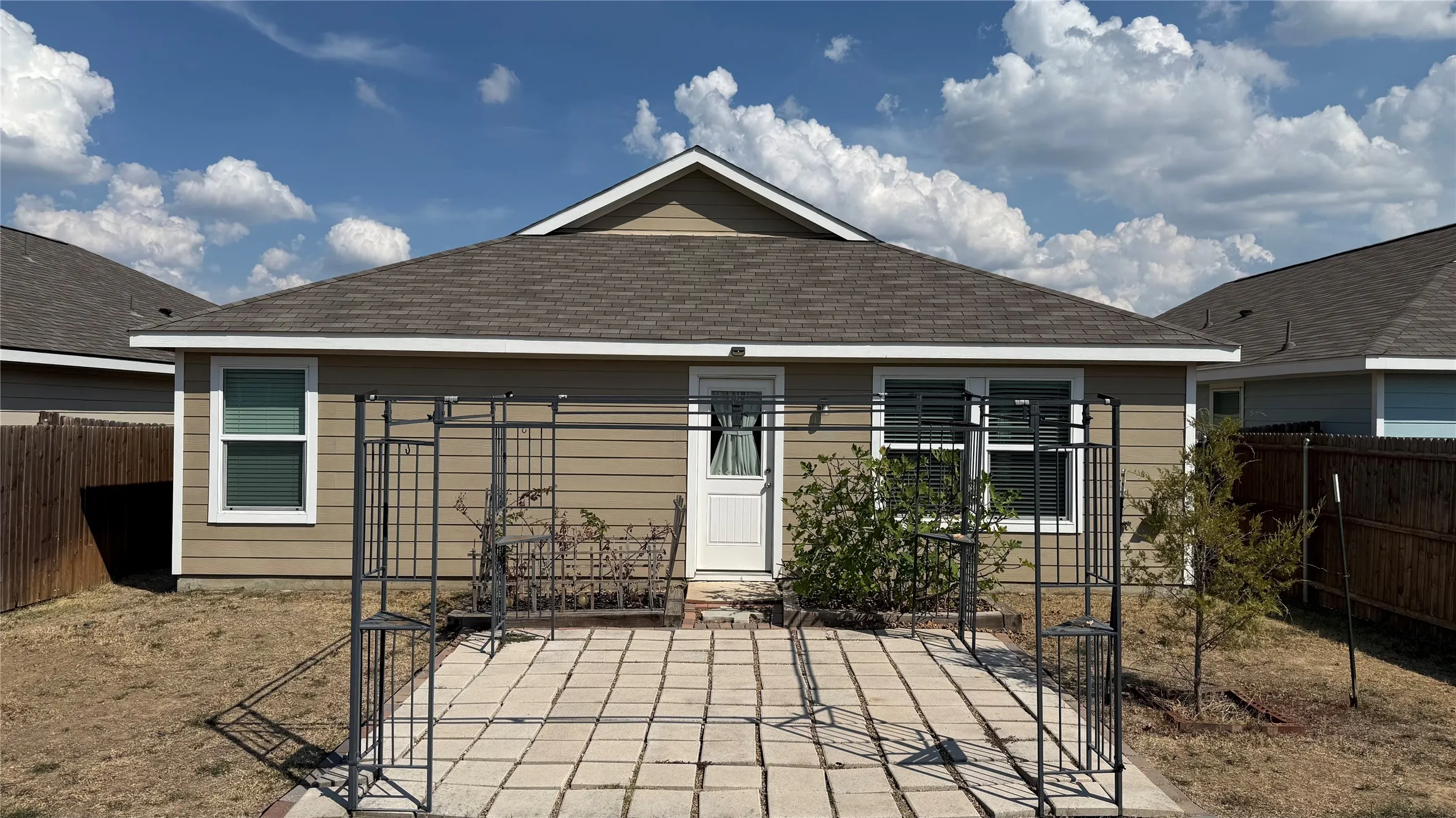 Rear exterior with tan siding and white trim, featuring a paved patio area