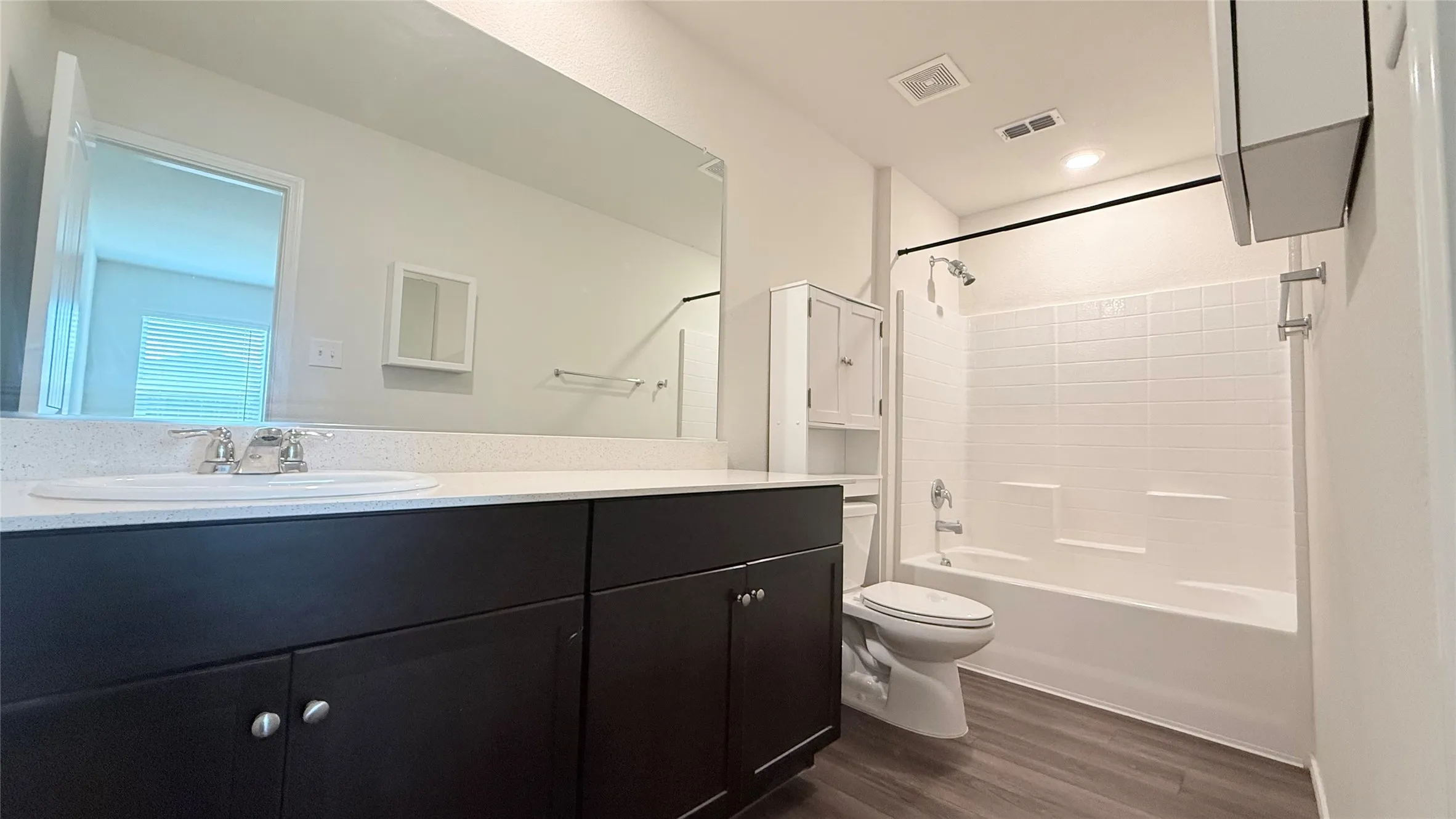 Dark wood-finish vanity with an integrated sink and light-toned countertop, large wall-mounted mirror, white subway-style shower tile, and wood-finish flooring