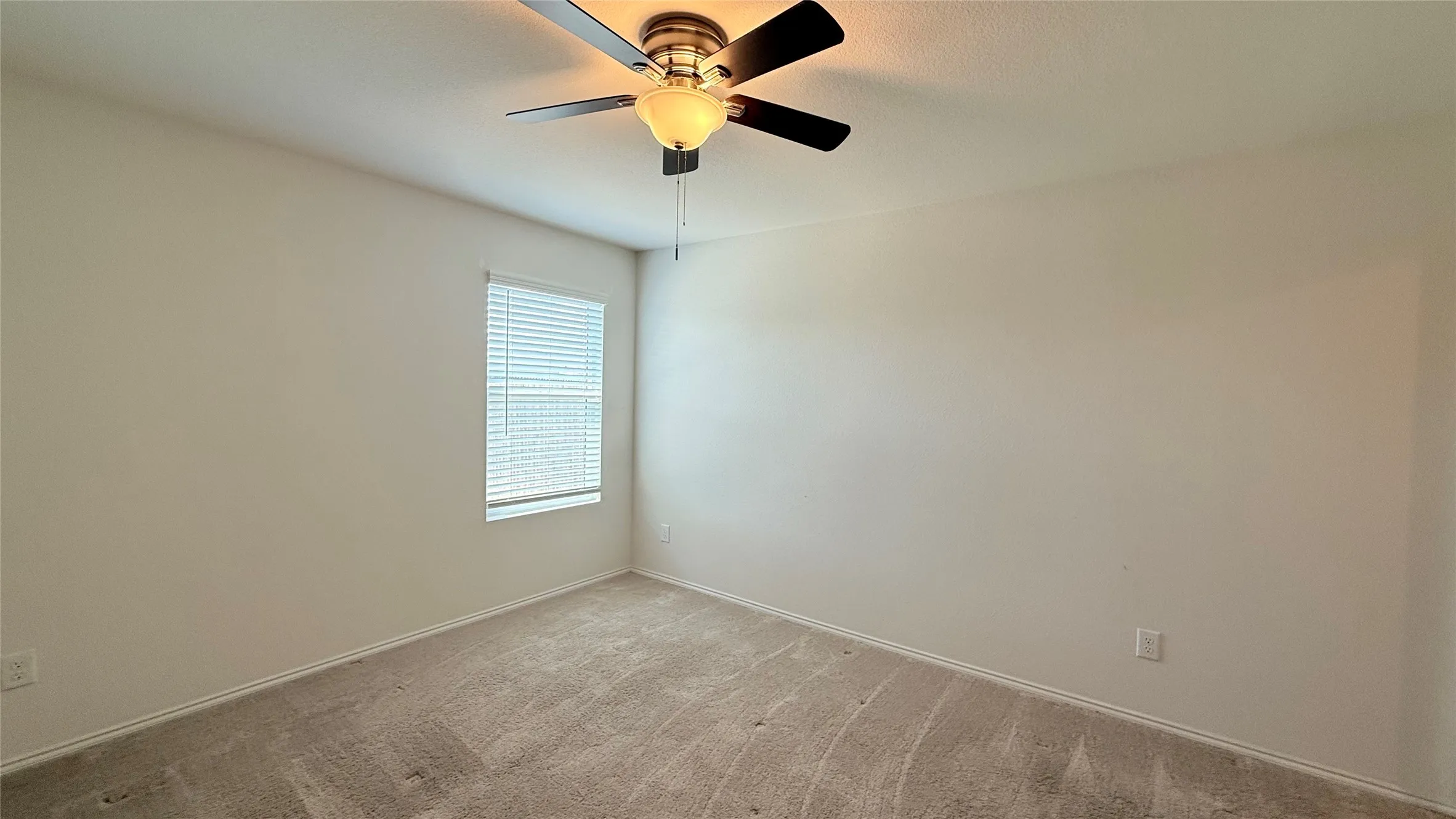 Neutral-toned carpeting, white walls, single window with blinds, and a ceiling fan with integrated lighting