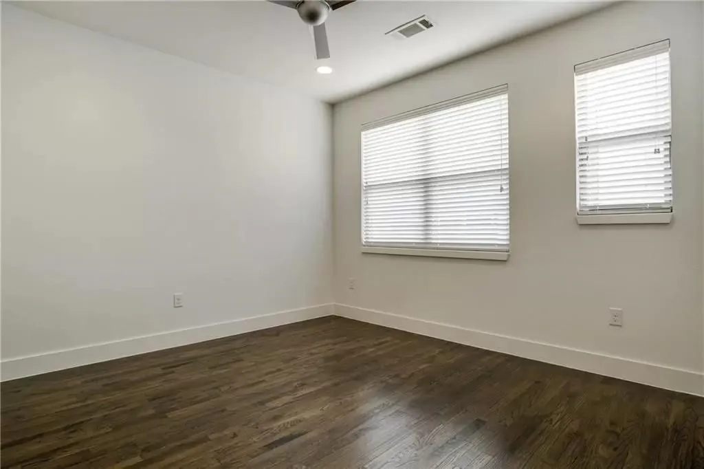 Dark wood-finish flooring, white walls, two windows with blinds, a ceiling fan, and recessed lighting