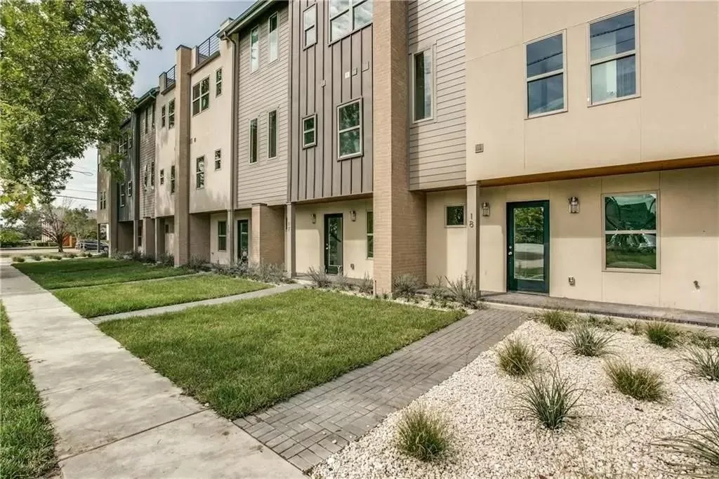 Contemporary townhome exterior with mixed material facade, paver stone walkway, mature landscaping, and an opaque glass-paneled entry door