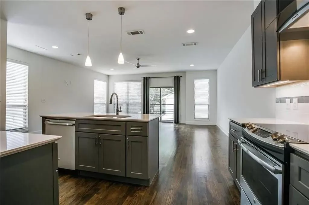 Kitchen island with built-in sink and stainless-steel dishwasher, complemented by wood-finish flooring, recessed lighting, and pendant light fixtures