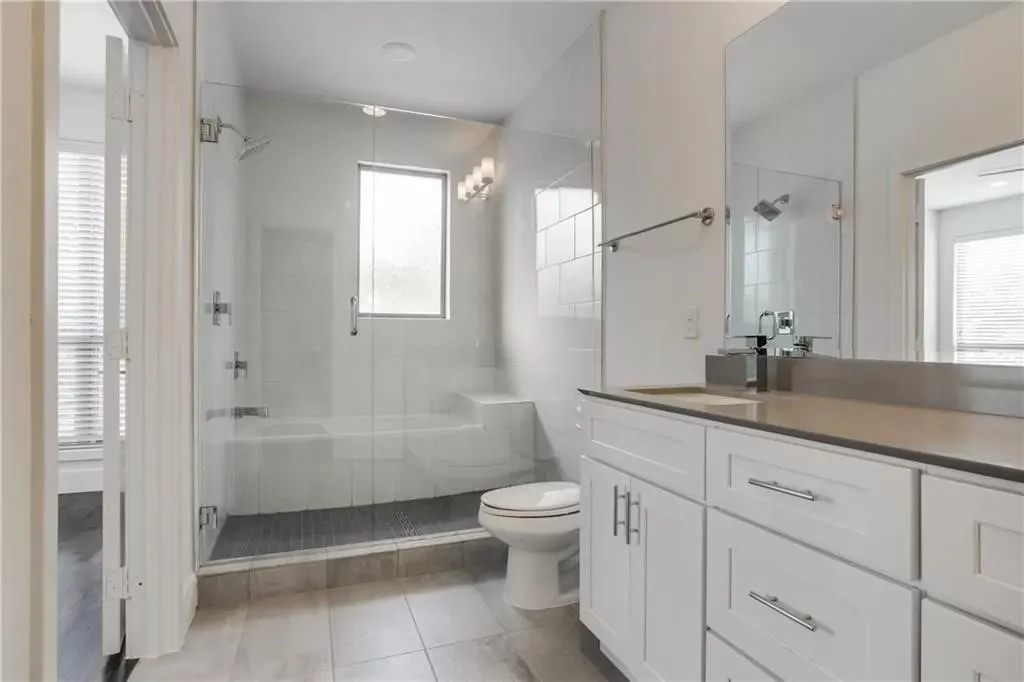 Spacious bathroom featuring a glass-enclosed shower, white vanity with ample storage, integrated sink, and large wall-mounted mirror