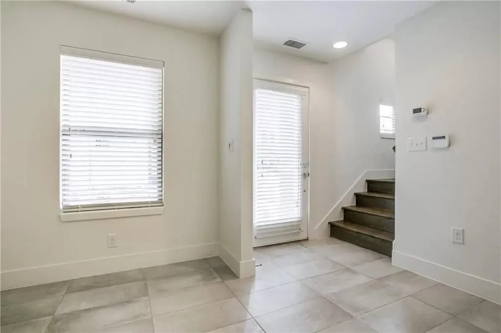 Ceramic tile flooring, white walls, window with blinds, door with blinds, and wood-finish staircase