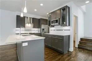 Kitchen featuring dark gray cabinetry, stainless steel appliances, a center island with sink, pendant lighting, and wood-finish flooring