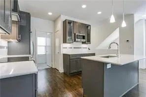 Kitchen featuring dark wood-finish cabinetry, light countertops, an integrated microwave, and a center island with a sink and pendant lighting