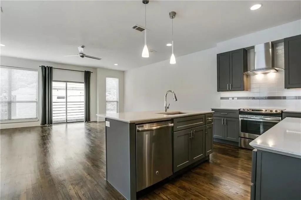 Dark wood-finish flooring throughout, complemented by a modern kitchen featuring stainless steel appliances, dark gray cabinetry, and light countertops
