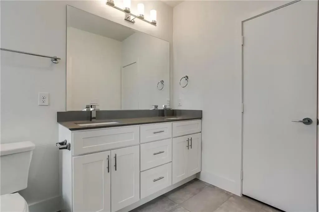 Dual vanity with a dark countertop, white shaker-style cabinetry, and integrated sinks