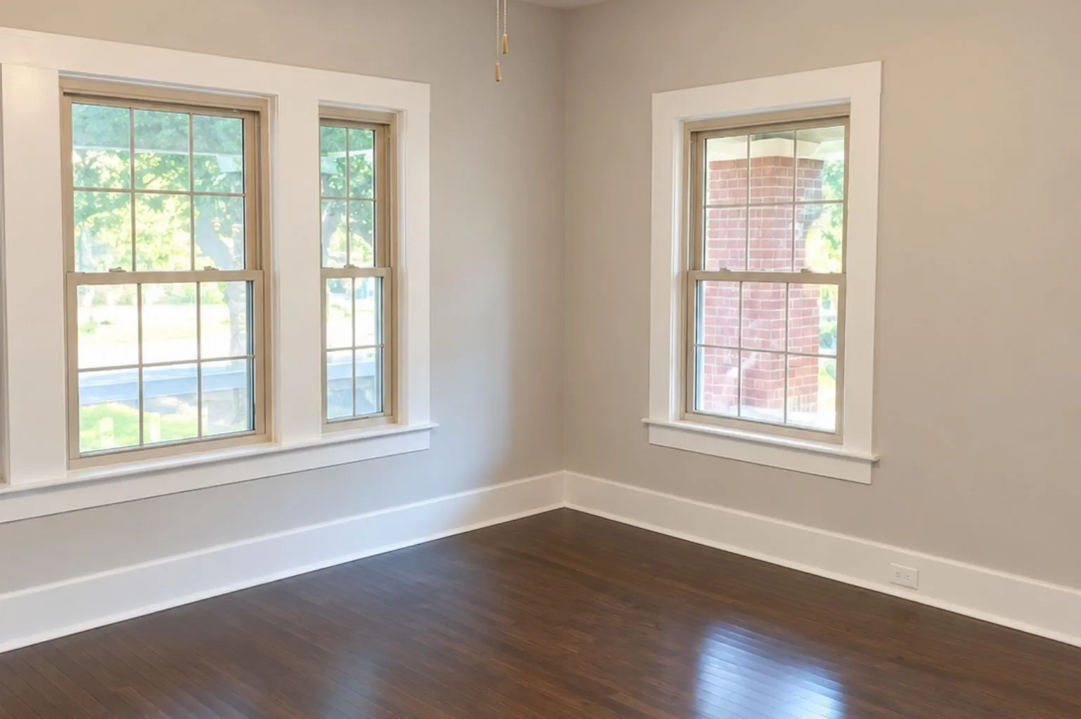 Bright bedroom featuring dark hardwood floors, three windows, neutral walls, white trim, and a ceiling fan.