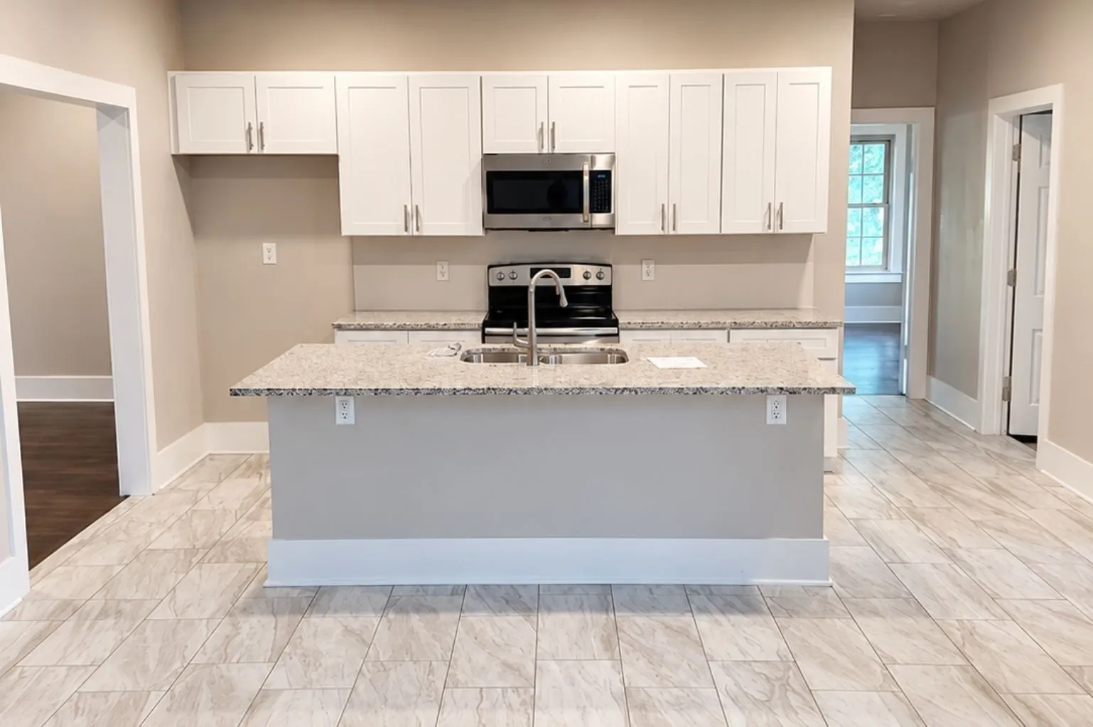 Open kitchen featuring white shaker cabinets, granite countertops, stainless appliances, large center island with sink, recessed lighting, and light tile flooring.