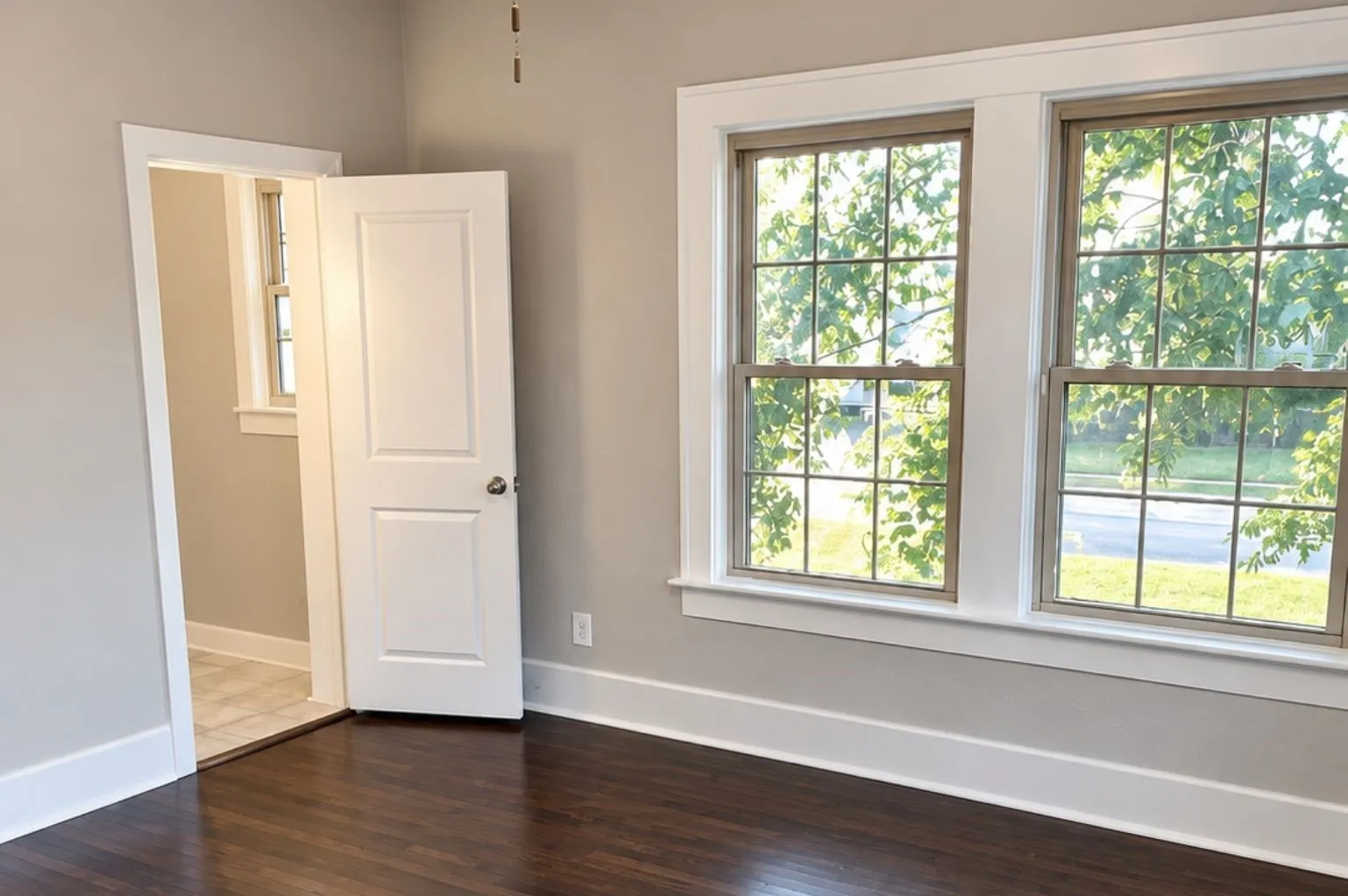 Empty bedroom featuring dark hardwood floors, two large windows, neutral walls, white trim, and a ceiling fan.