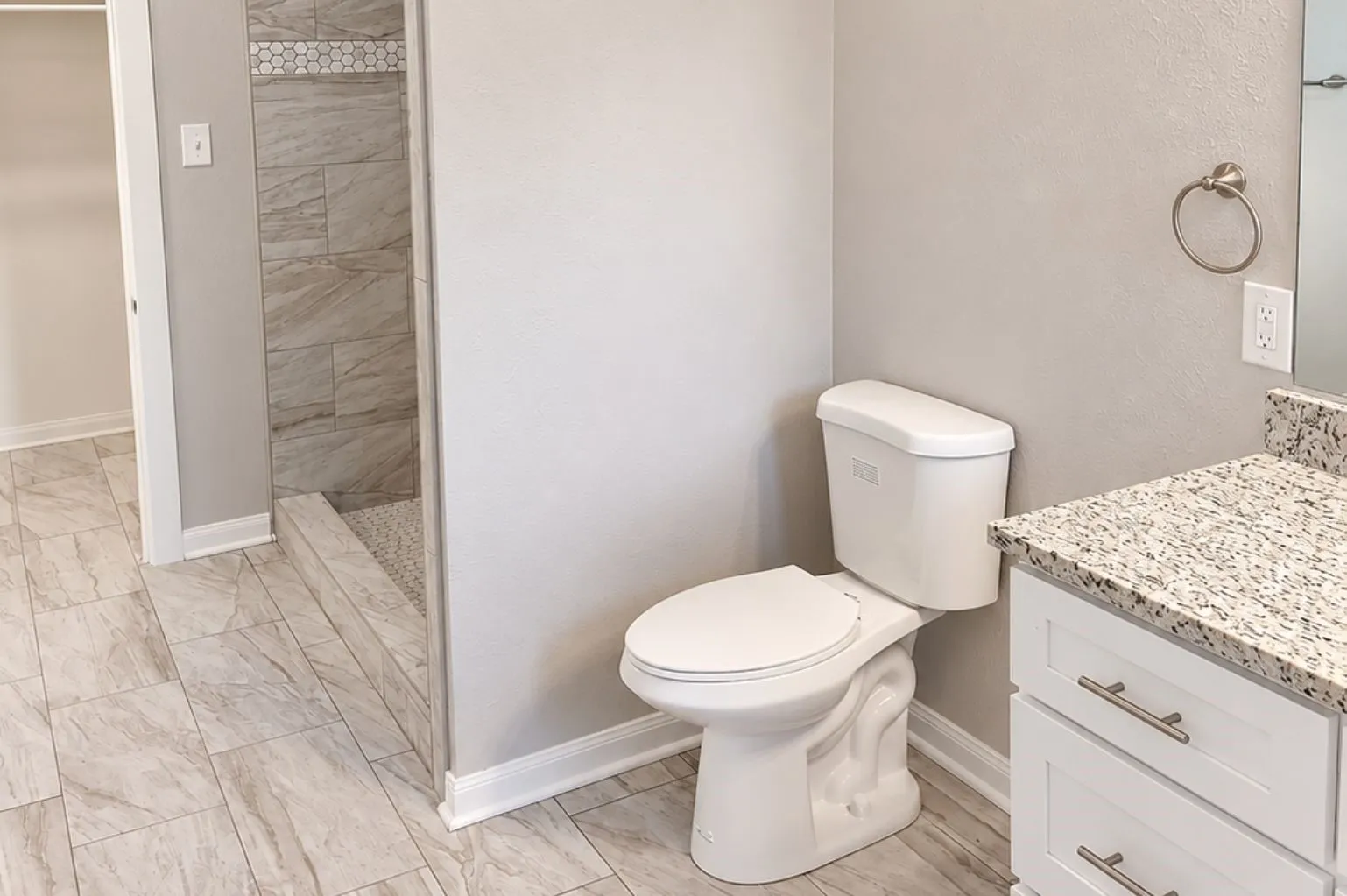 Updated bathroom featuring a white vanity with granite countertop, toilet, tiled walk-in shower, neutral finishes, and light tile flooring.