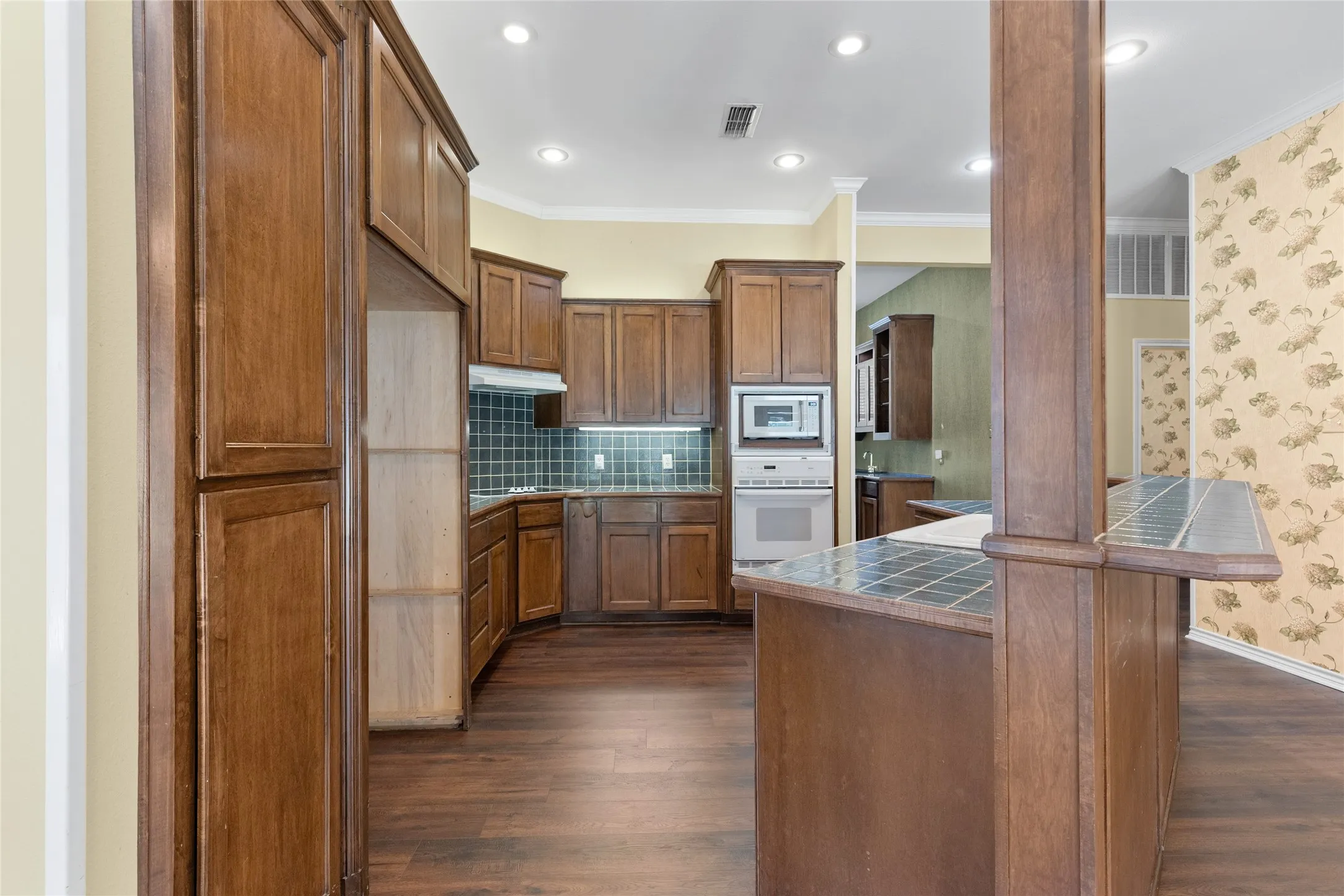 Spacious kitchen with island and breakfast bar, pantry cabinet, plus a large pantry closet, wet bar area, and warming oven near the pantry.