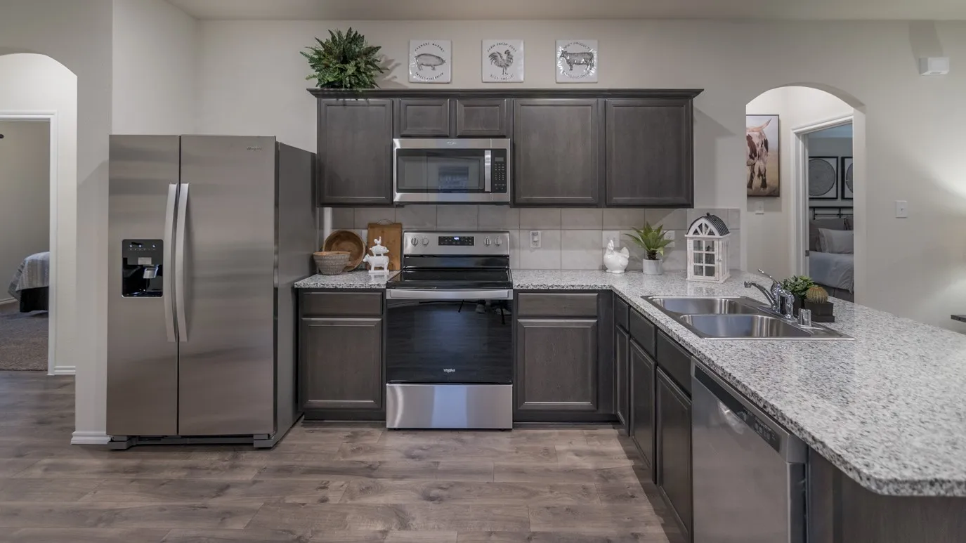 Well-appointed kitchen featuring wood-finish flooring, dark wood cabinetry, stainless steel appliances, and light-toned speckled countertops with a tile backsplash