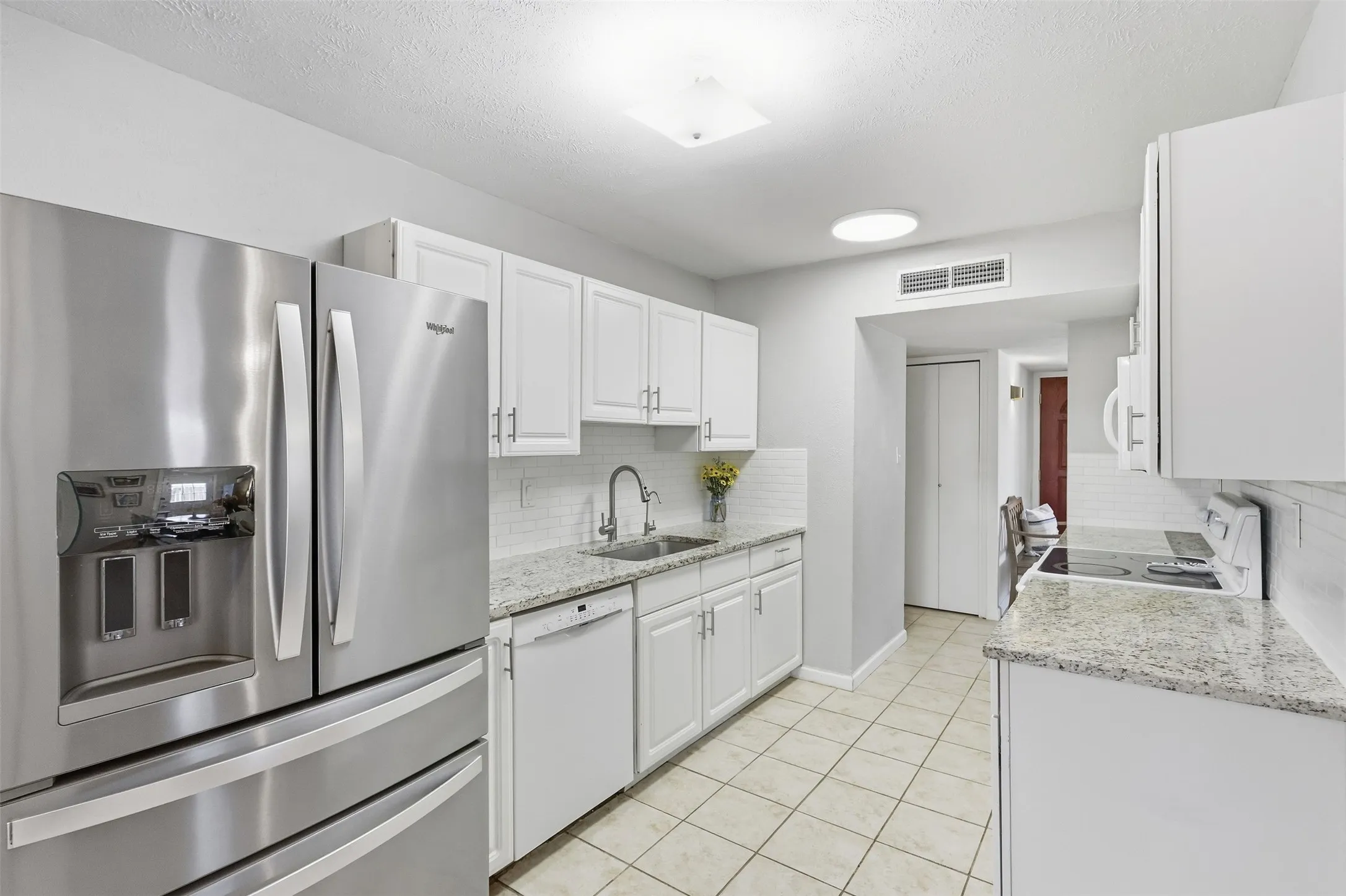 Bright kitchen with white cabinetry, stainless steel fridge, and plenty of workspace.