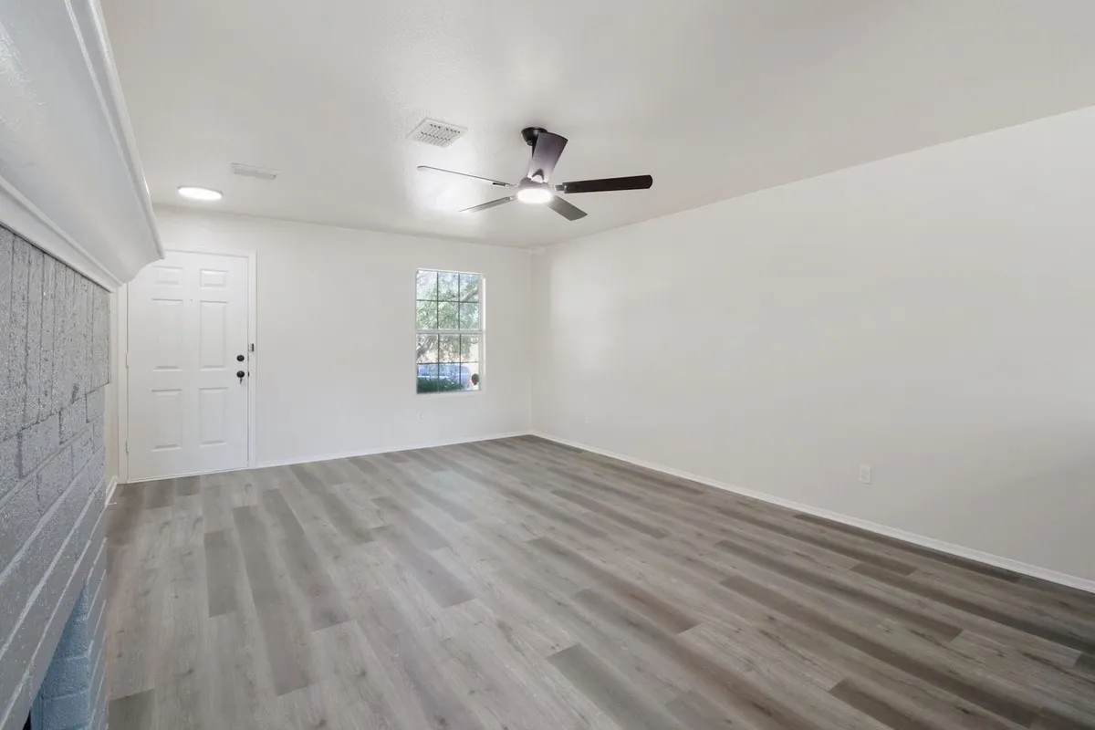 Spacious room featuring wood-finish flooring, a ceiling fan, a window, and a white paneled door