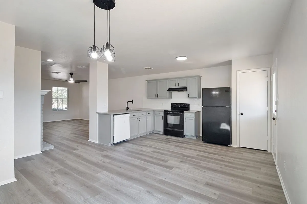 Open-concept living space with wood-finish flooring, recessed lighting, and a modern kitchen featuring grey cabinetry and dark appliances