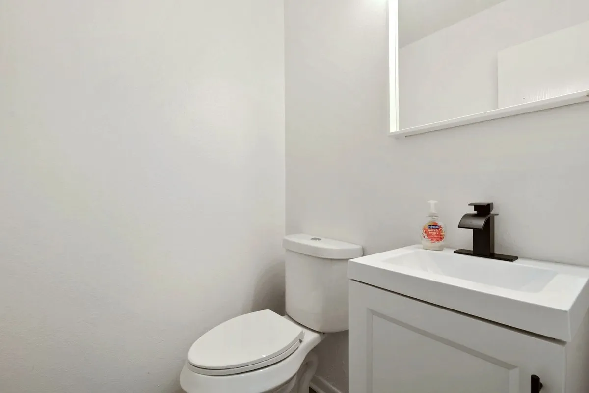 White vanity with an integrated basin sink, black single-handle faucet, and illuminated mirror
