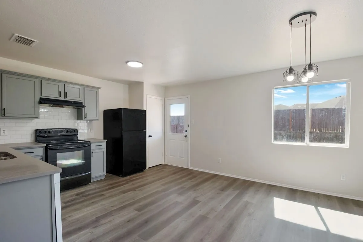 Open-concept living space with wood-finish flooring, gray shaker-style cabinetry, white subway tile backsplash, and a modern multi-bulb pendant light fixture
