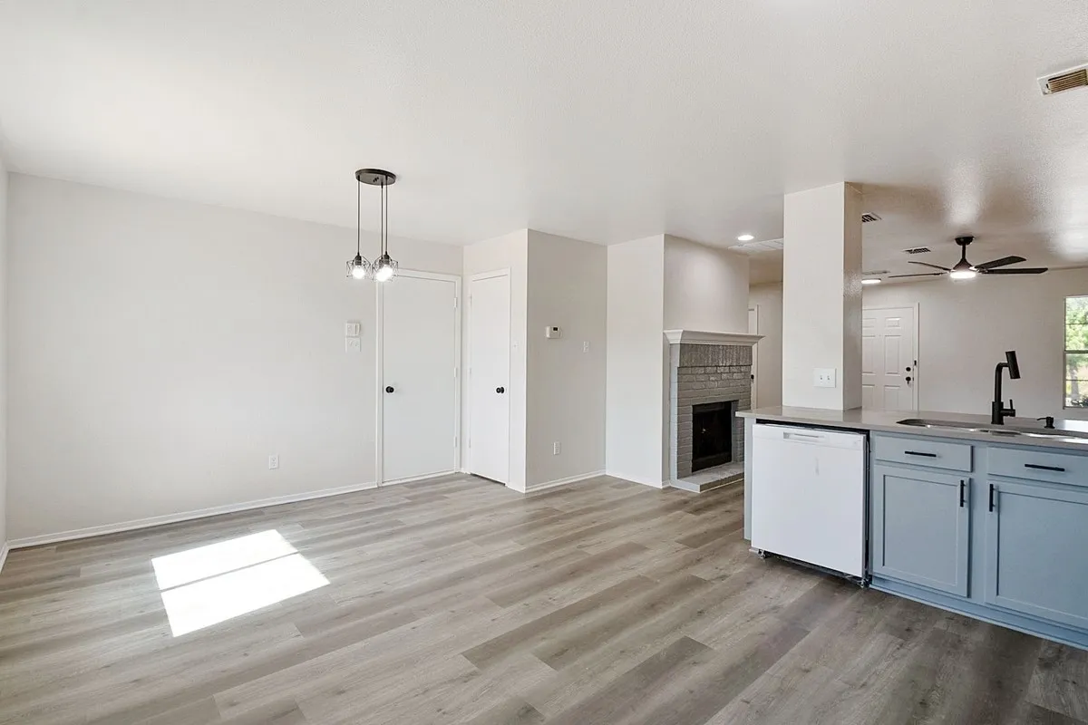 Wood-finish flooring, recessed lighting, fireplace with a brick surround, light gray cabinetry, and a black gooseneck faucet