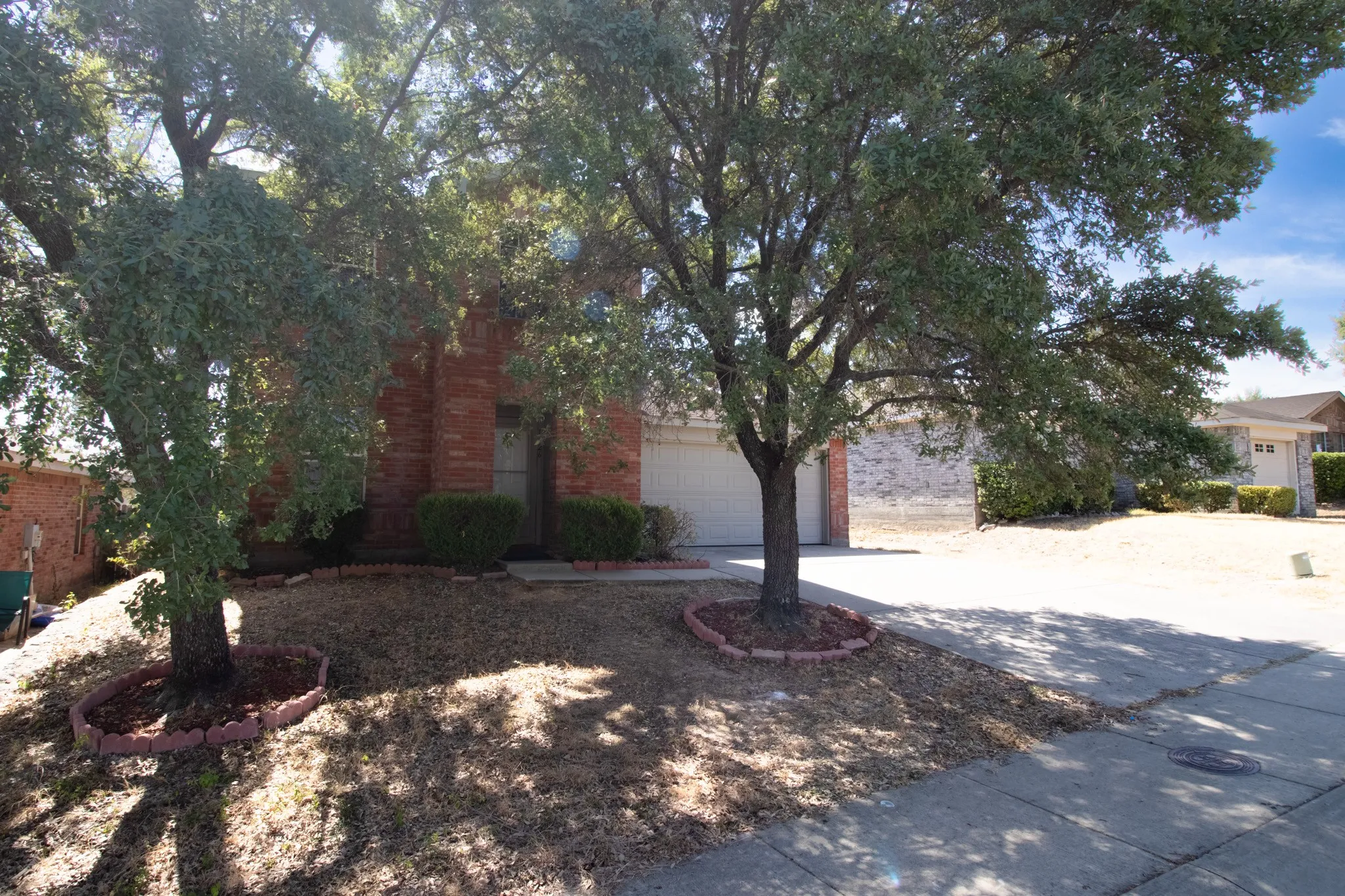 Brick exterior with an attached garage, mature trees, and a concrete driveway