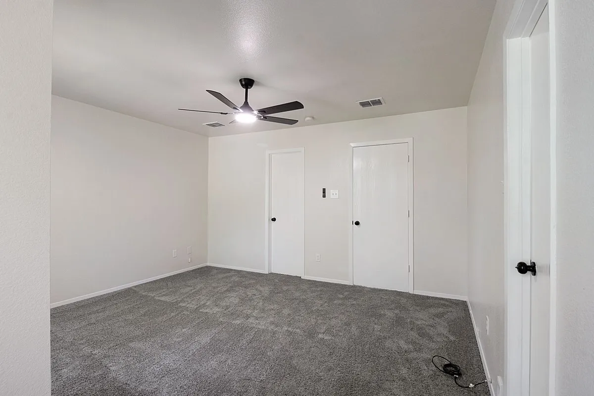 Spacious room featuring gray carpet, a ceiling fan with integrated lighting, and multiple interior doors