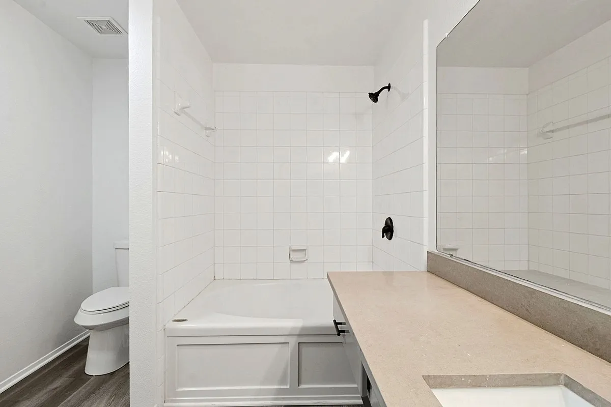 White subway tile shower surround with a built-in tub, black shower fixtures, and a vanity with a light-toned countertop