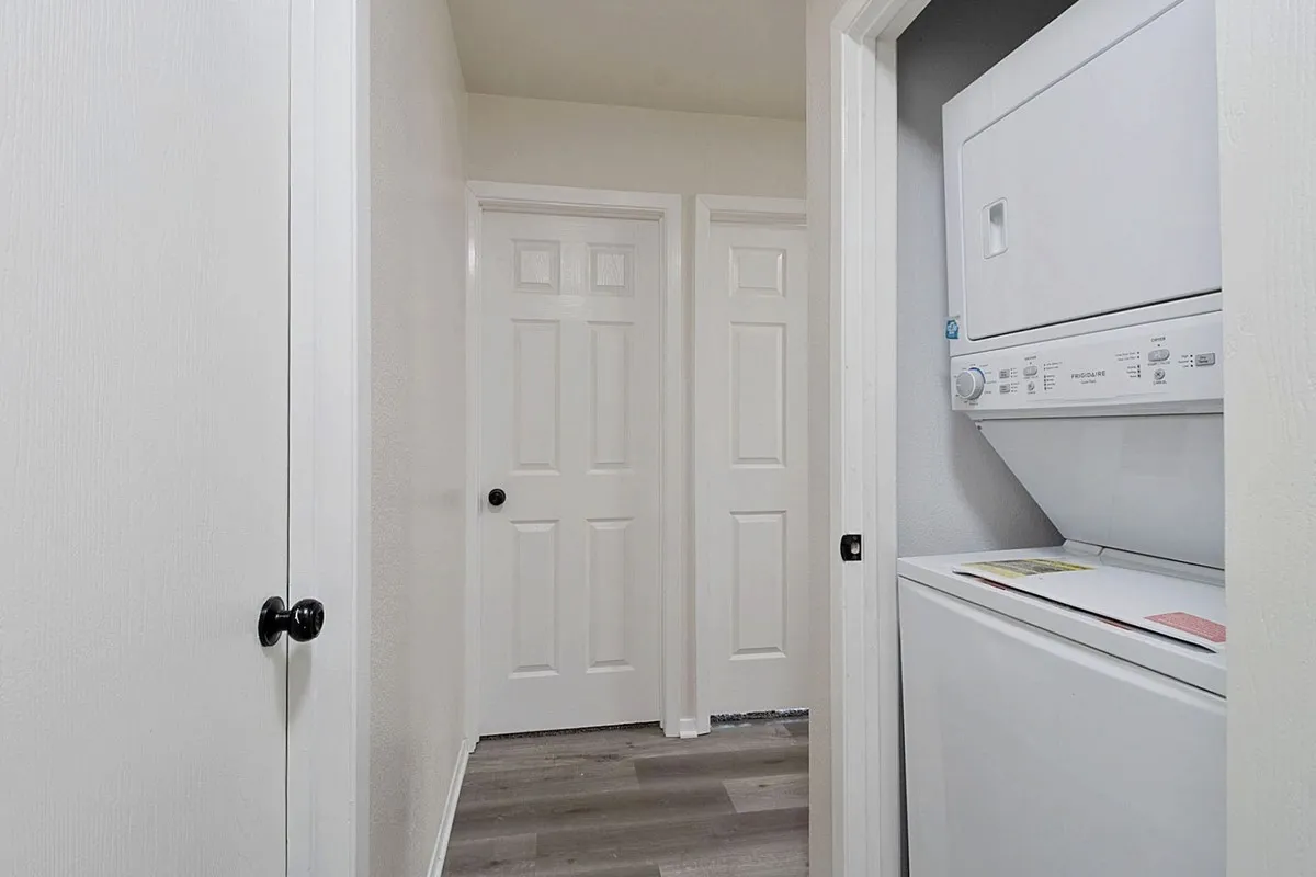 Hallway with light-toned wood-finish flooring, white walls, and white paneled doors with matte black hardware