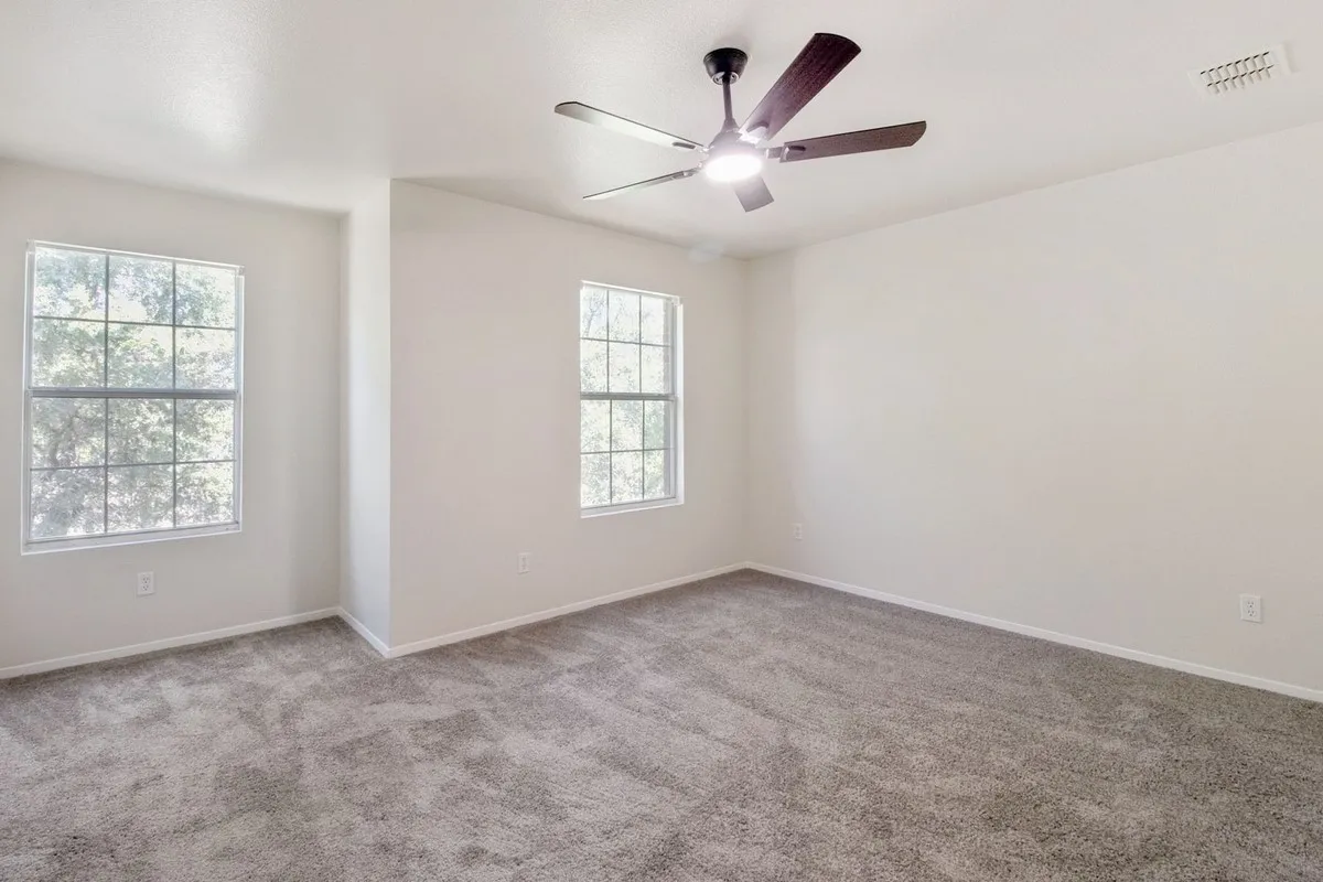 Spacious room featuring neutral carpeting, light-toned walls, two multi-pane windows, and a ceiling fan with integrated lighting