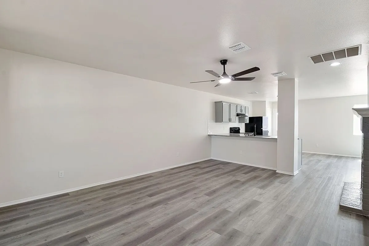 Open-concept living space featuring wood-finish flooring, a ceiling fan with integrated lighting, and a partial wall separating the kitchen area