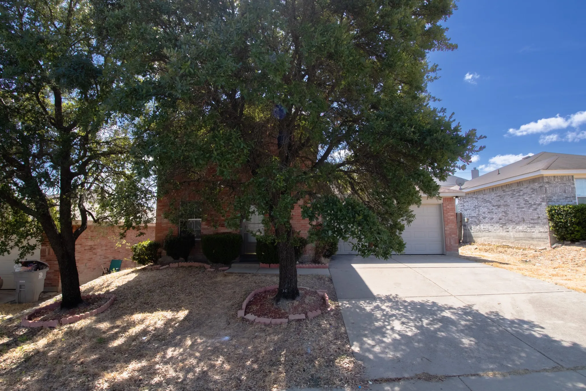 Brick exterior with a two-car garage, concrete driveway, and mature trees