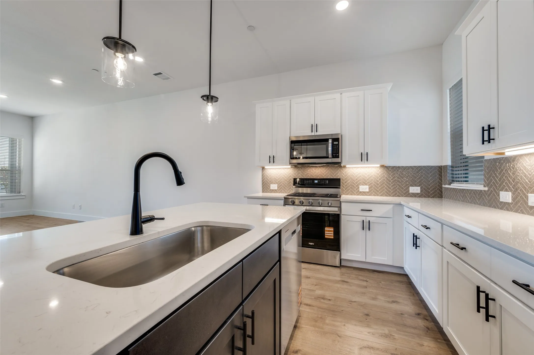 A generous center island with an undermount sink and contemporary black faucet offers plenty of workspace, while stainless steel appliances, under-cabinet lighting, and dramatic black accents complete the polished look.