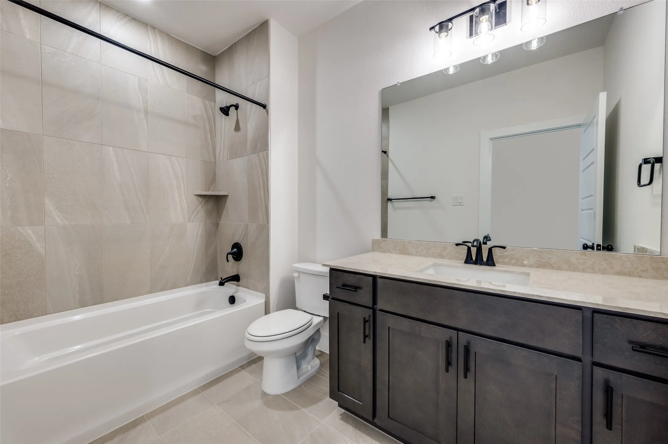 Stylish full bathroom featuring a spacious vanity with abundant cabinetry, generous counter space, and a large mirror. The tub and shower combination is surrounded by elegant floor-to-ceiling tile, while sleek black fixtures and hardware add a modern, sophisticated finishing touch.