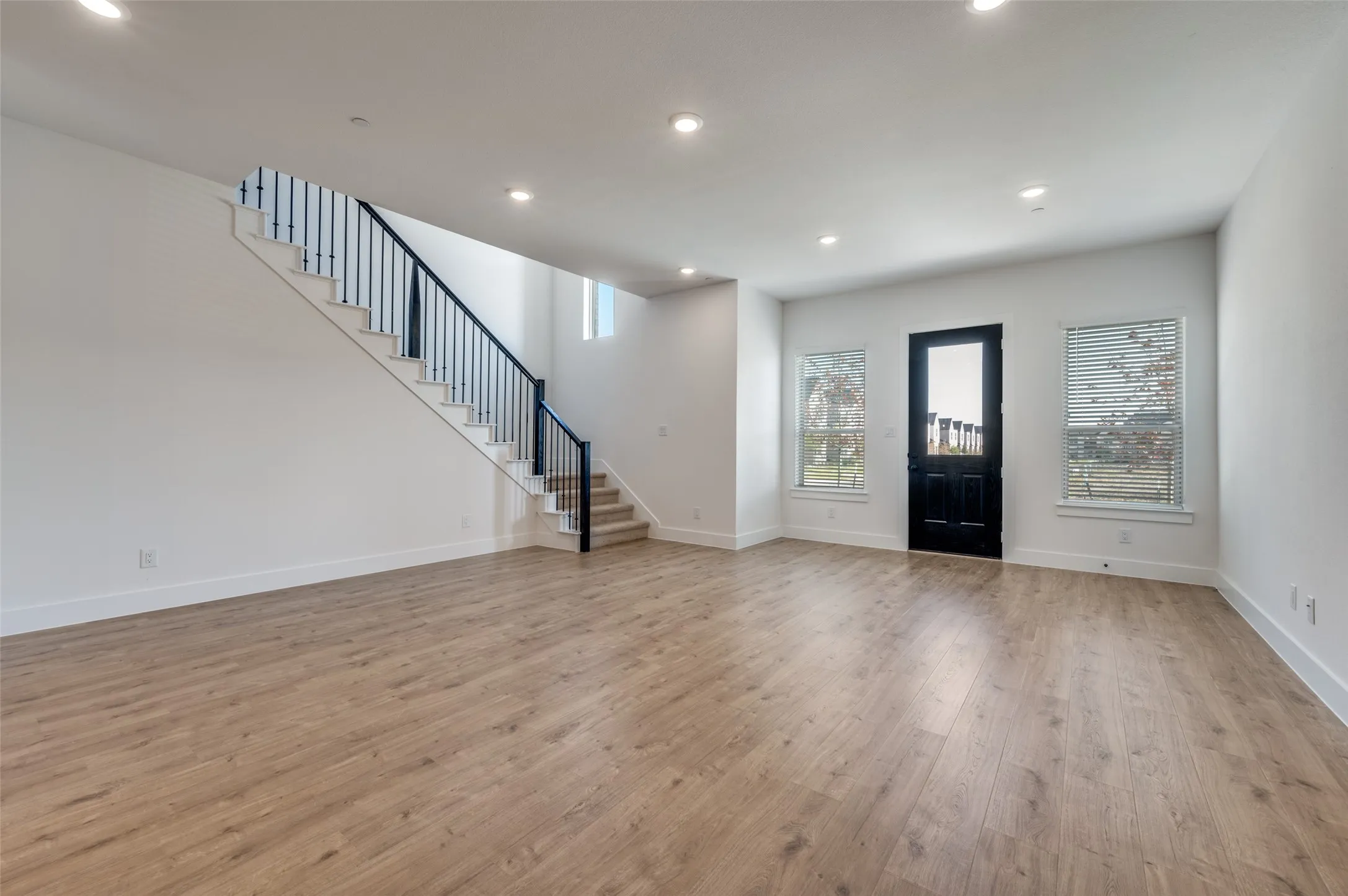 Bright and inviting open floor plan featuring beautiful engineered hardwood floors, recessed lighting, and an abundance of natural light. The spacious layout offers a seamless flow for everyday living and entertaining, while the modern staircase with sleek black iron railing adds a stylish architectural touch.