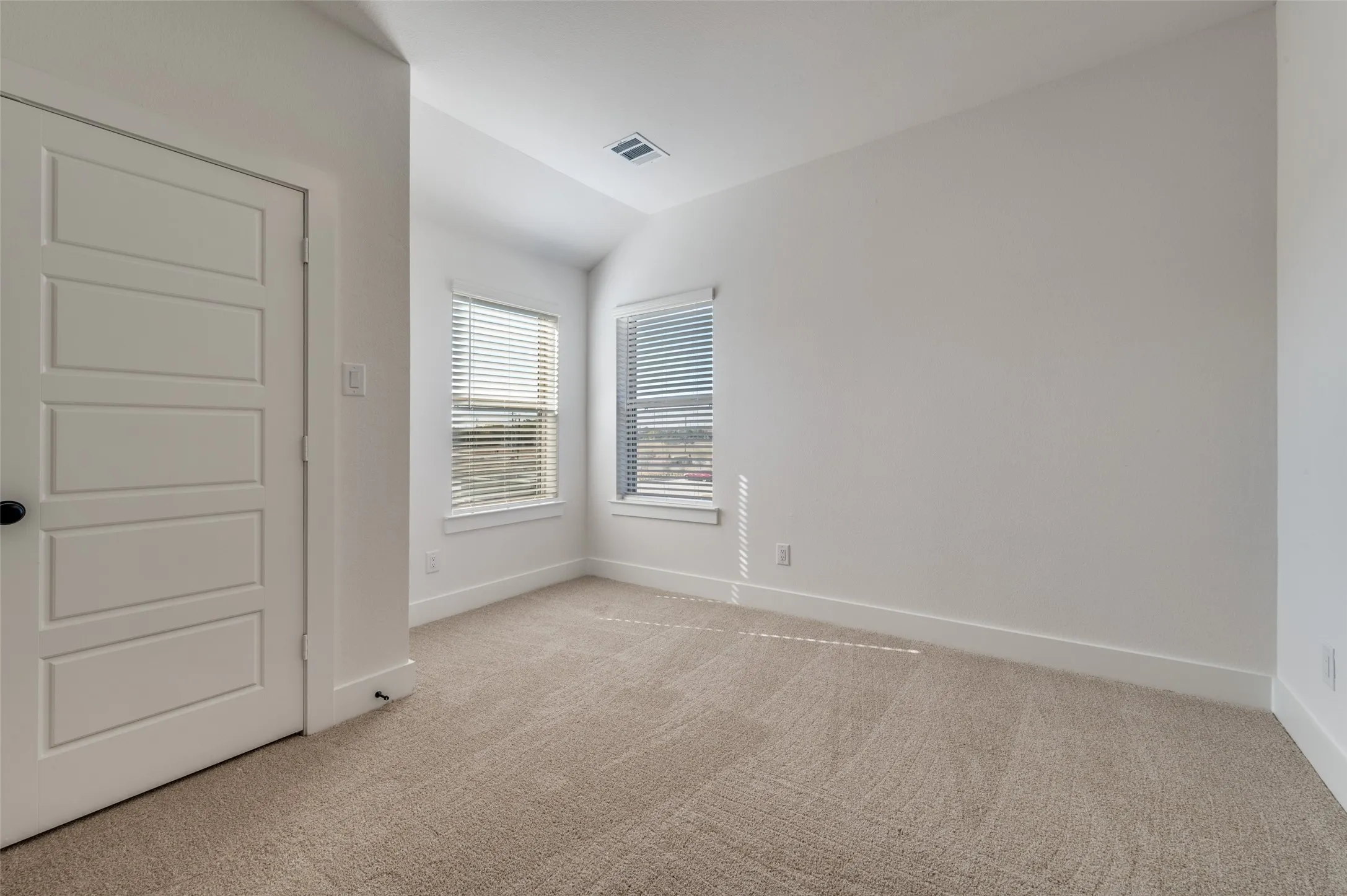 Bright and spacious secondary bedroom featuring plush carpeting, neutral finishes, and multiple windows that fill the space with natural light. The generous layout offers plenty of flexibility for family, guests, or even a private home office.