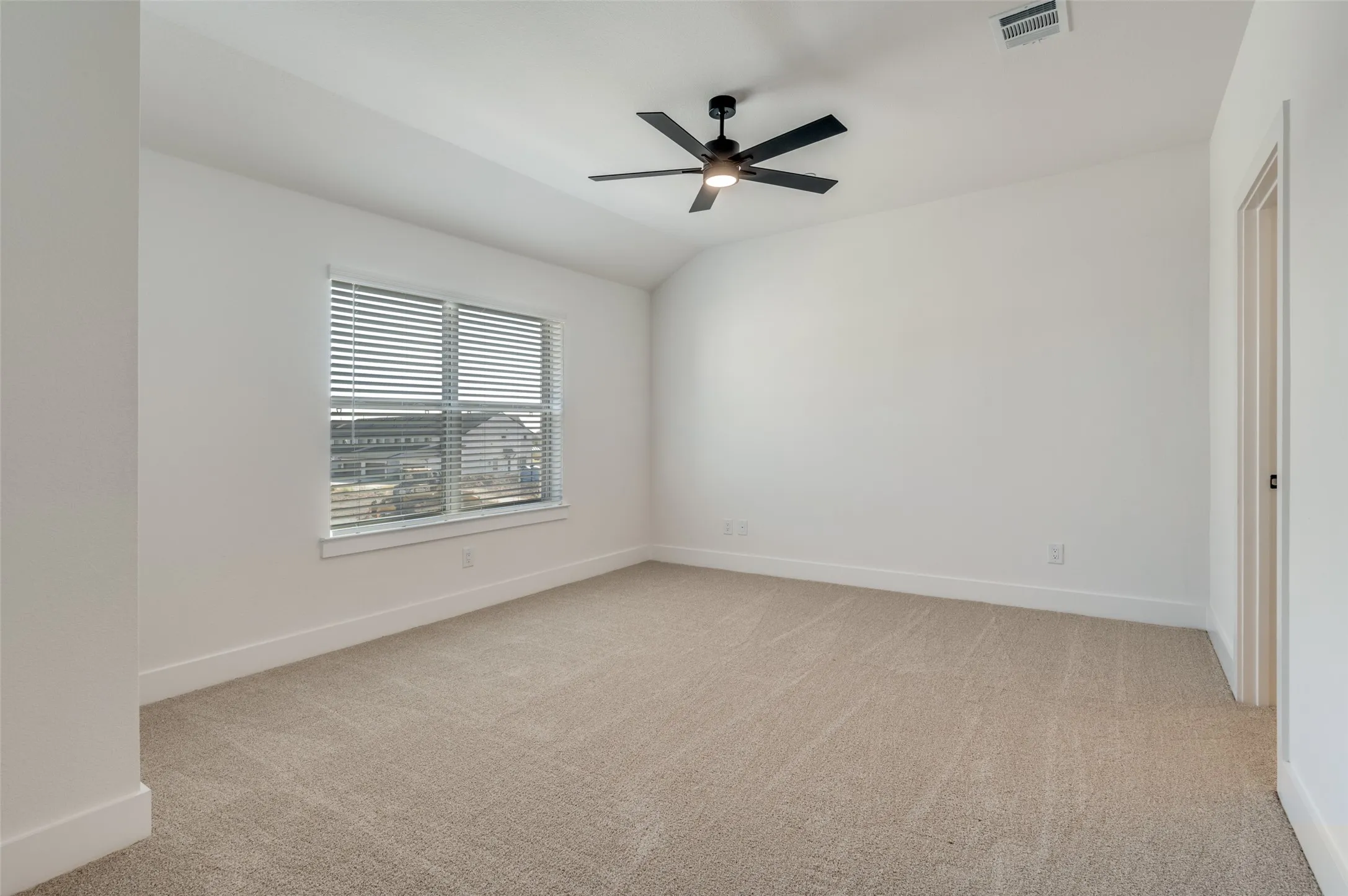 Spacious primary suite featuring plush carpeting, a vaulted ceiling, and a modern ceiling fan. A large window fills the room with natural light, while the generous layout offers plenty of space for a sitting area. A private ensuite bath completes this comfortable and inviting retreat.