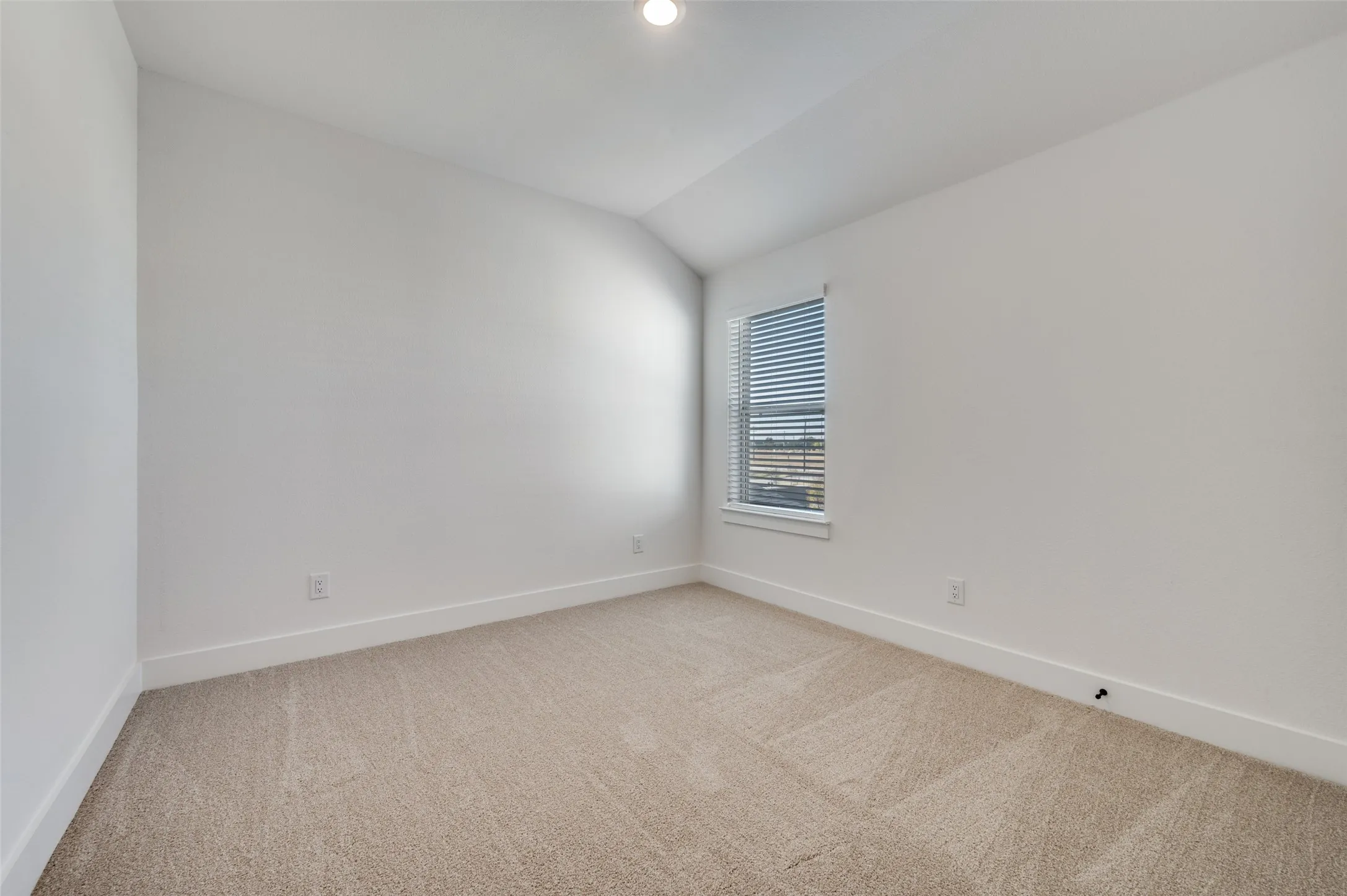 Spacious secondary bedroom featuring plush carpeting, a vaulted ceiling, and a large window that fills the room with natural light. The neutral finishes create a bright, comfortable space ready to be personalized for family or guests.